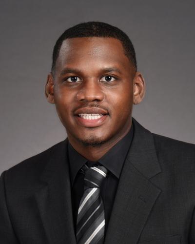 Image of a black male from the chest up wearing a dark colored suit and smiling